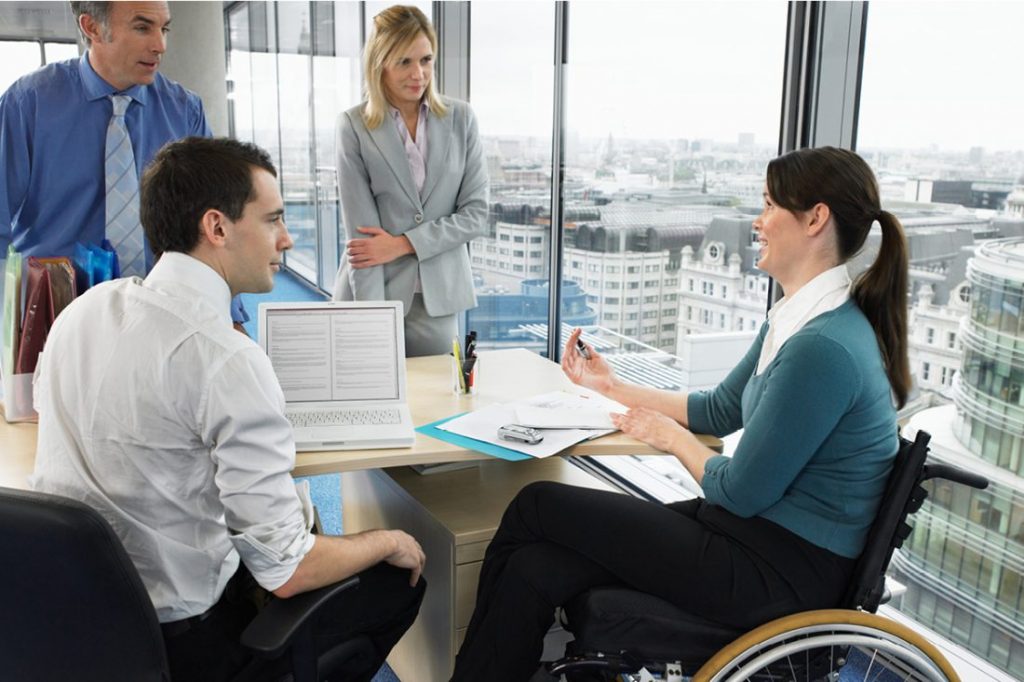 Three people round the table in the workplace and one lady on a wheelchair