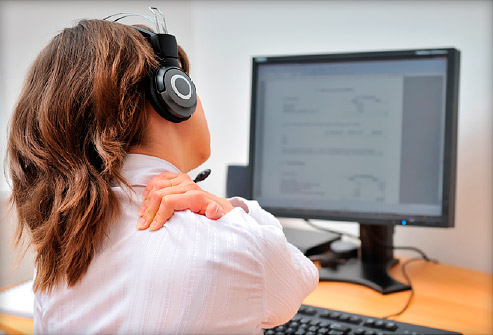 A girl sitting at her desk working with her computer and her neck is hurting