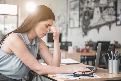 A girl sitting at her desk and holding her forehead