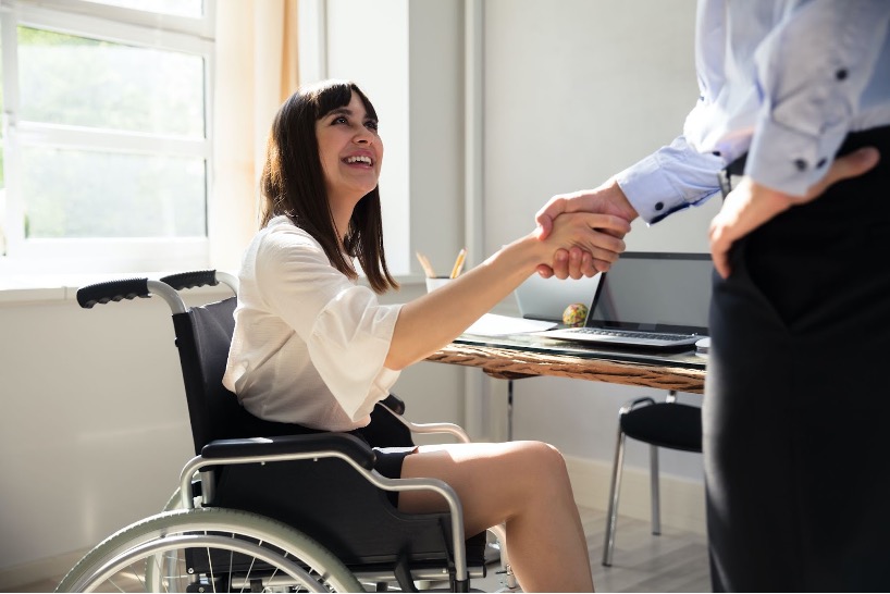 A woman on a wheelchair smiling and shaking hand with a man
