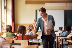 Happy teacher and schoolgirl giving high five in classroom.